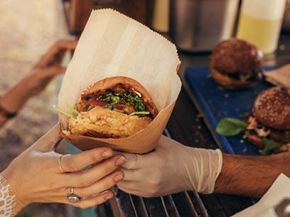 Woman hand reaching for a burger at food truck. Closeup of food truck salesman serving burger to female customer.